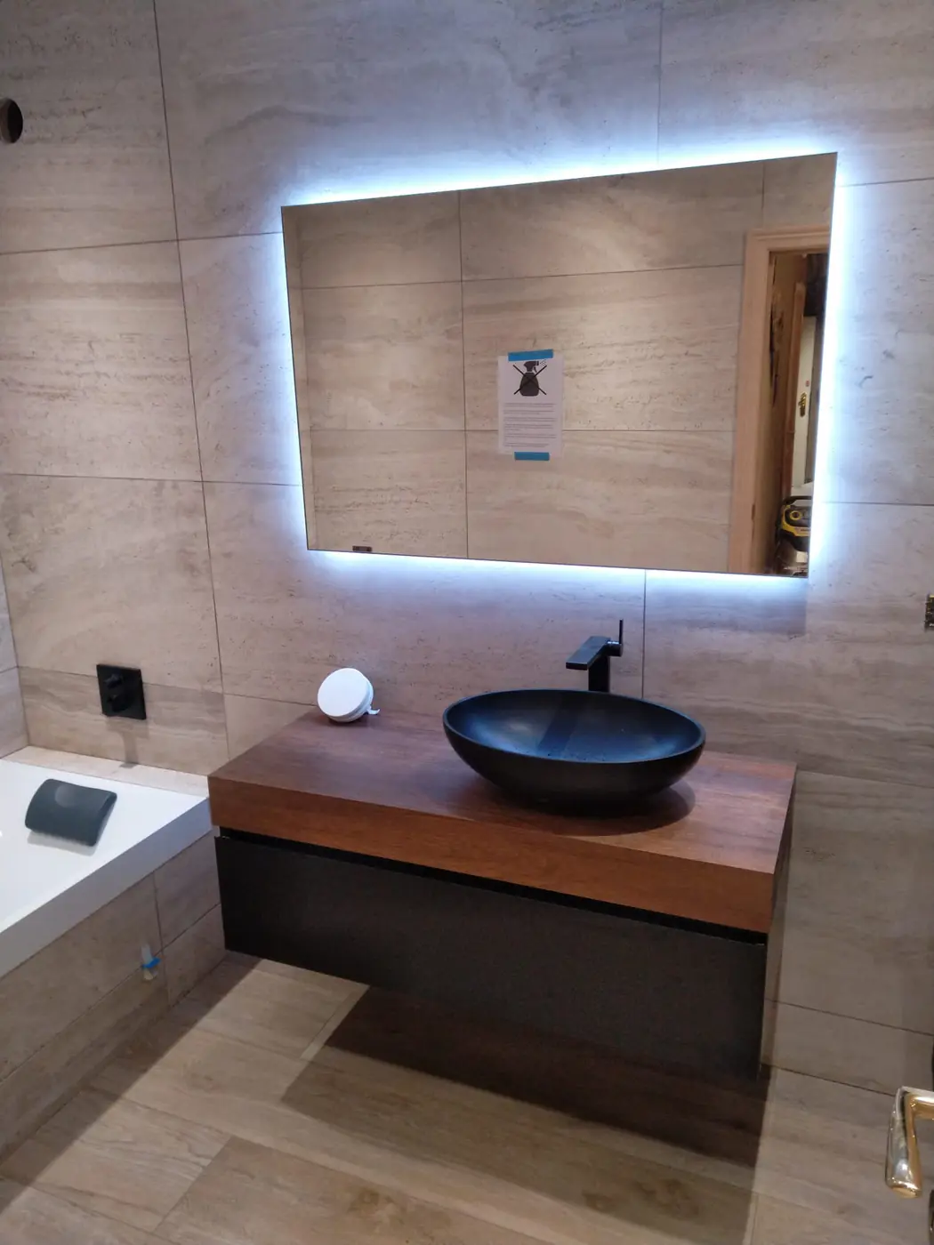 Meuble vasque en bois, vasque noire et miroir LED dans une salle de bain rénovée